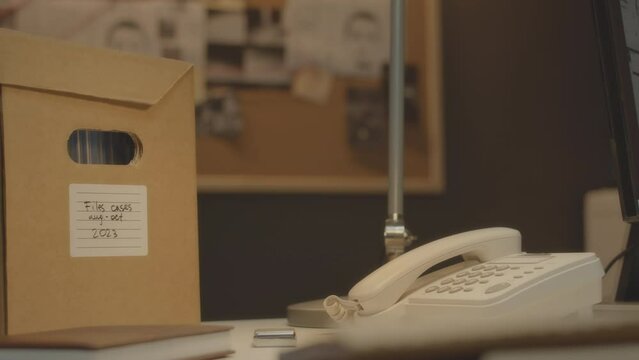 No people shot of cardboard box with evidence files and materials on detective work desk in his office with investigation corkboard hanging on wall in blurred background