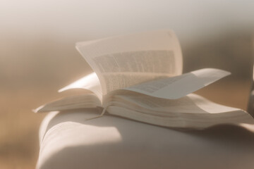 Bible on top of a chair in a shepherd with dry and yellowed grass. Winds leafing through the pages of the Bible book and white cloth swaying in the wind.