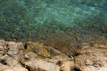 Image of the crystal-clear waters of the Mediterranean Sea in the Costa Brava, with the reflection of the sun on its waves breaking against the rocks.