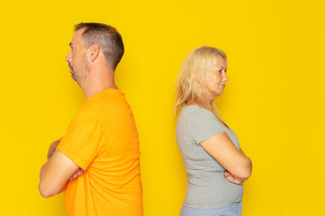 Portrait of a real Caucasian couple in their 40s having an argument, they are angry and turn their backs on each other. Isolated on yellow background. - obrazy, fototapety, plakaty
