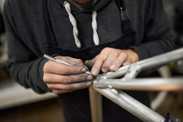 Hands of an unrecognizable hispanic man removing paint residue from a bicycle frame as part of the process of a bike renovation work made at his workshop.