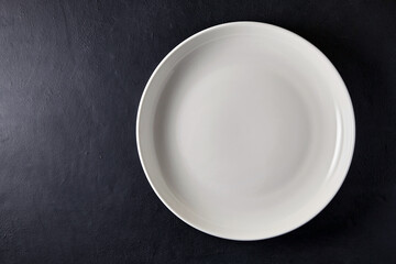 Empty white ceramic plate on a black stone table. Top view with copy space
