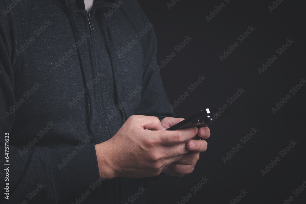 Poster man in hood jacket typing on smartphone in dark background. using mobile phone for texting, messagin