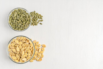 Top view of two bowls with peeled and unshelled pumpkin seeds of light green colour with white outer husk, contains fat, protein, dietary fiber served on wooden table with copy space used in culinary