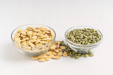 Side view of two bowls with peeled and unshelled pumpkin seeds of light green colour with white outer husk, contains fat, protein, dietary fiber served on wooden table used as ingredient or snack
