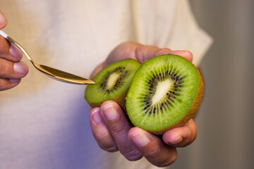 Senior woman holding in her hand a ripe green kiwi fruit cut in half ready to eat. Healthy fruits...