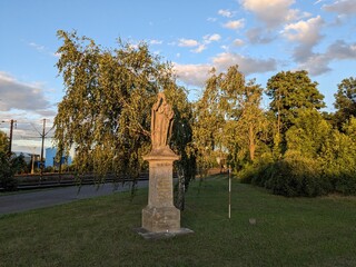 Obraz premium Sandstone statue of a saint located near the railway station in Nymburk, showing historic religious sculpture, weathered stone, and cultural heritage in an urban public space.