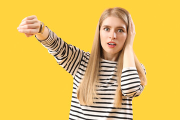 Stressed young woman looking at wristwatch on yellow background. Deadline concept