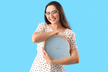 Young woman with clock on blue background. Deadline concept