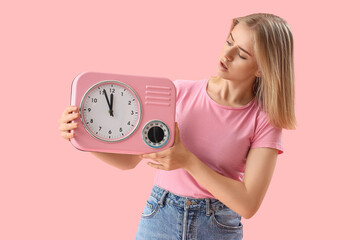 Stressed young woman with clock on pink background. Deadline concept