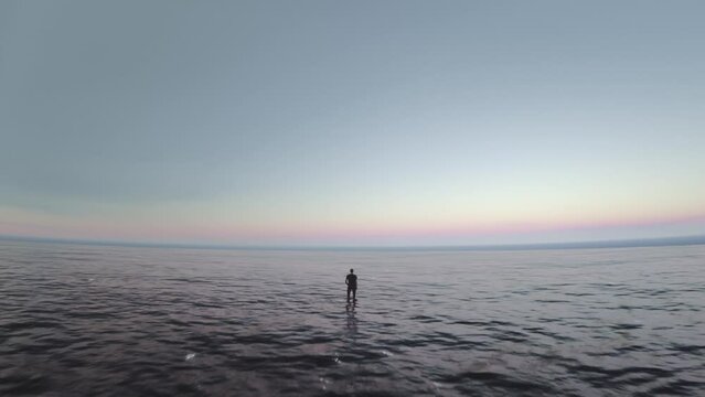 Drone video of a single man standing in the middle of the sea looking at the horizon. End of the world. Meditation, perspectives, loneliness, facing the odds alone concept. Endless ocean, infinity. 