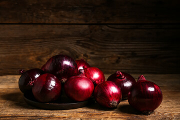 Plate with fresh red onions on wooden background