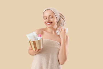 Pretty young woman with bath supplies on beige background