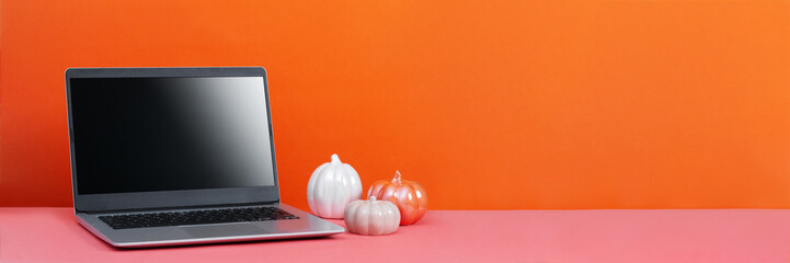 Blank screen laptop on table with minimal autumn or fall season decor, orange colors, seasonal business concept. Decorative ceramic pumpkins and open laptop web banner