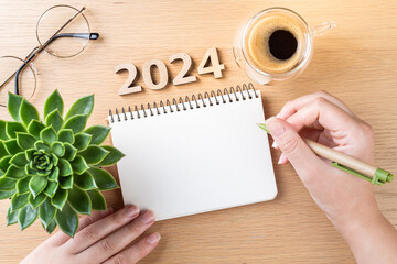 New year resolutions 2024 on desk. 2024 goals - hands and notebook, coffee cup, plant on wooden...