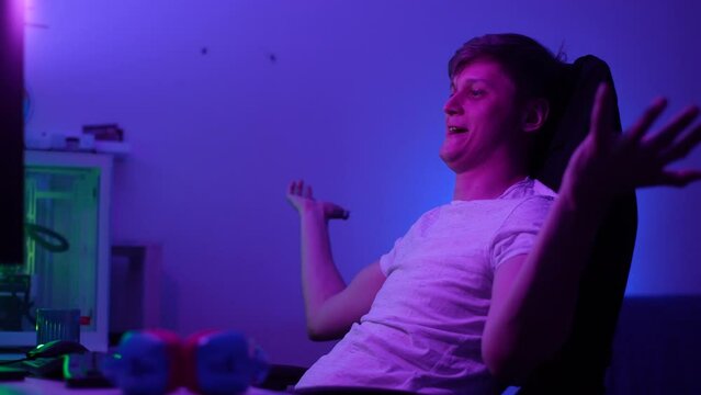 Side view of sad male gamer playing home in neon lights. Frustrated young man losing checking game results after arcade round. Focused gamer looking computer screen resting in cyberspace room, slowmo.