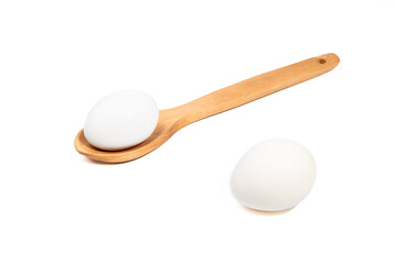 Uncooked chicken eggs in a wooden spoon and on the edge on white background.