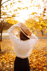 Beautiful woman in casual clothes and hat walking, enjoying the weather in the autumn golden park. Autumn mood. Fashion, style concept.