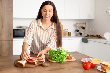 Obraz na płótnie Canvas Young woman making tasty sandwich in kitchen