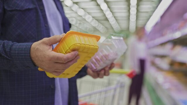 A close-up of the pensioner's hands holding semi-finished meat products packed in plastic packaging. An elderly man in a supermarket. 
