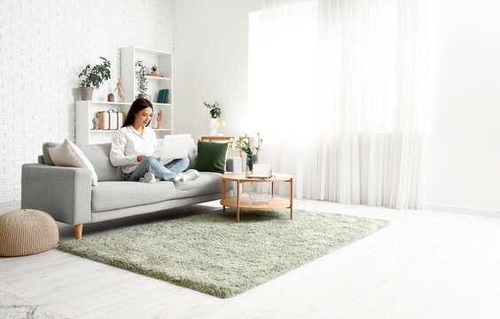 Beautiful Young Asian Woman With Laptop Sitting On Sofa In Living Room