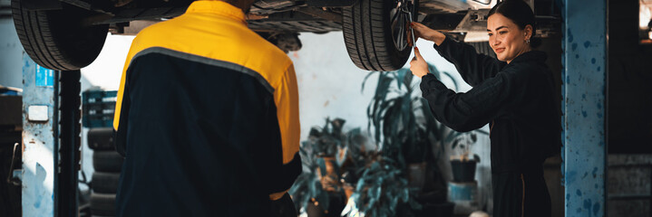 Vehicle mechanic conduct car inspection from beneath lifted vehicle. Automotive service technician in uniform carefully diagnosing and checking car's axles and undercarriage components. Panoram Oxus - obrazy, fototapety, plakaty