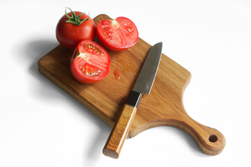 Solid oak wooden cutting board, chopped red tomato and sharp knife on a white background. The concept of preparing a summer salad in the kitchen. Photo.