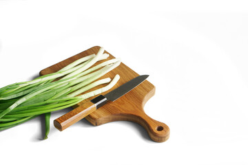Sharp knife, vintage solid oak wooden cutting board and chopped green onions on a white background. Concept for making a rustic summer green salad. Photo. Selective focus