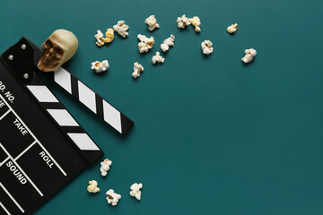 Composition with tasty popcorn, clapperboard and skull for Halloween celebration on green background - obrazy, fototapety, plakaty