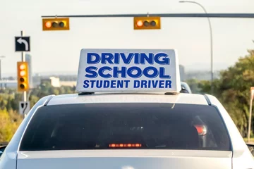 Foto op Canvas An instructional vehicle, bearing a prominent driving school student driver sign affixed to its roof, diligently navigates a well-lit thoroughfare as part of the educational process. © oasisamuel