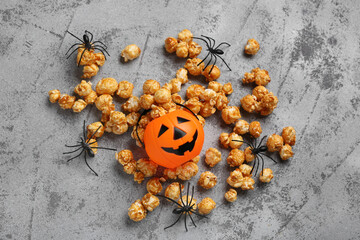 Caramel popcorn with Halloween pumpkin and spiders on grey grunge background