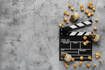 Movie clapperboard with caramel popcorn and Halloween skulls on grey grunge background