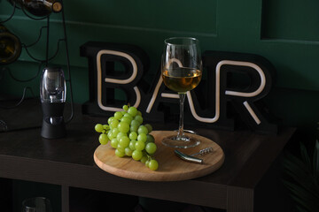 Board with glass of tasty wine and grapes on table, closeup