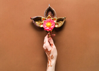Female hand with diya lamps and lotus flower for celebration of Divaly on brown background