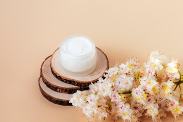 Cream jar and Horse chestnut flowers on wooden stand on beige table. Natural organic cosmetics concept. Top view
