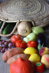Round straw bag with seasonal fruit and vegetable on wooden background. Late summer or early autumn. Selective focus.
