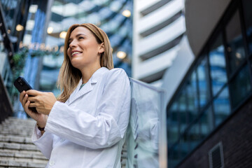 A female doctor on a break uses the phone to send a message. Caucasian young woman doctor smiling...