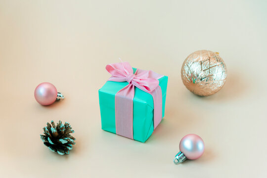 Teal blue gift box with pink bow, Christmas balls and pine cone on beige background