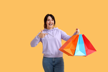 Beautiful happy woman with shopping bags on yellow background