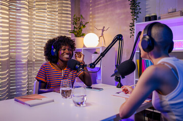 The multiracial young women are sitting in a podcast studio and laughing