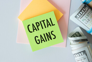 Capital Gains Text on Green Sticker attached to notepad with money dollars