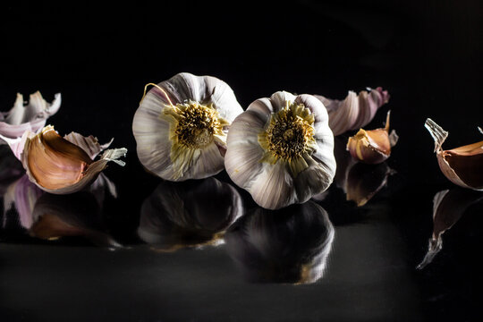 Algumas cabe&ccedil;as de alho sobre uma superf&iacute;cie preta reluzente.