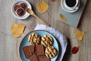 Cup of tea or coffee, plate with cookies and chocolate, dried oranges, bowl of grapes, vintage books, pumpkins and autumn leaves on the table. Autumnal hygge. Top view.