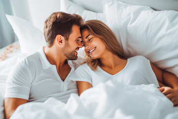 Beautiful young couple smiling and laying in bed with white sheets