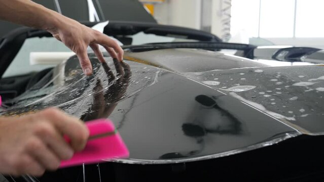 Close up of paint protection film installation on front bumper of modern luxury car. PPF is polyurethane film applied to car surface to protect the paint from stone chips, bug splatter, and abrasion.