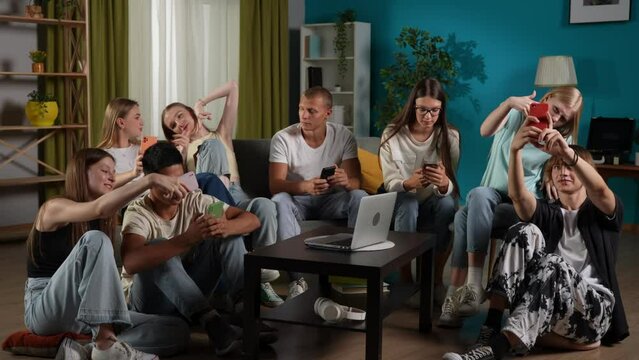 Full-size video of a group of teens, young people, friends sitting on a couch and floor around the table, using their smartphones, taking selfies, pictures.