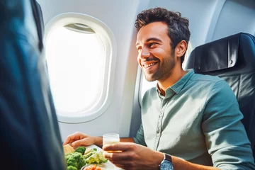Rolgordijnen Handsome young man eating a plane meal at a window seat, enjoying a meal on a plane ride © VisualProduction