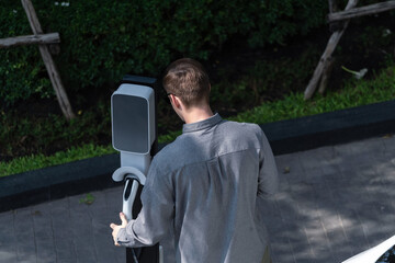 Young man travel with EV electric car charging in green sustainable city outdoor garden in summer...