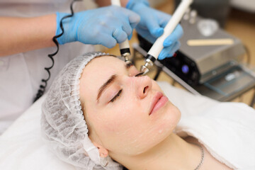 Obraz na płótnie Canvas cosmetologist conducts microcurrent facial therapy for a young woman using a device in a beauty salon. Hardware cosmetology, skin care, rejuvenation, regeneration.