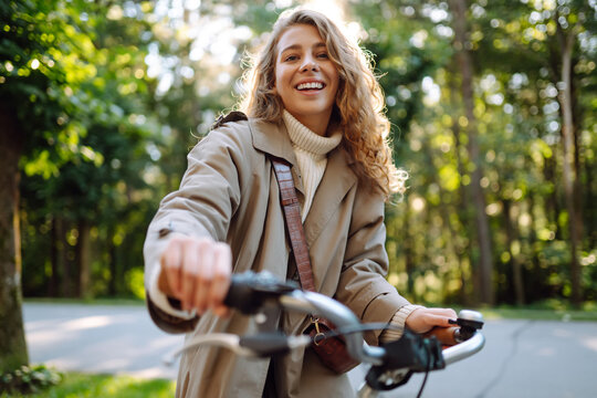 Young smiling woman in casual stylish clothes rides a bicycle in a sunny park. Active urban healthy lifestyle concept.